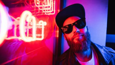 Ein Mann mit Sonnenbrille und Mütze sitzt an einem Fenster.