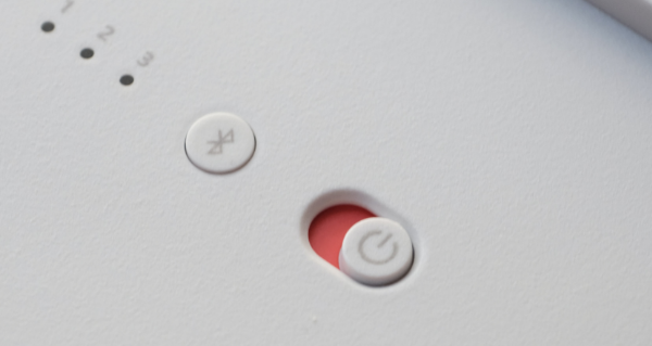 An- und Ausschalter und Bluetooth Schalter auf einem weißen Gerät befindet sich ein An- und Ausschlater, welcher auf rot geschaltet ist und ein Bluetooth Schalter. Links davon befindet sich eine Nummerierung von 1-3 mit jeweils einem schwarzen Kreisen darunter.