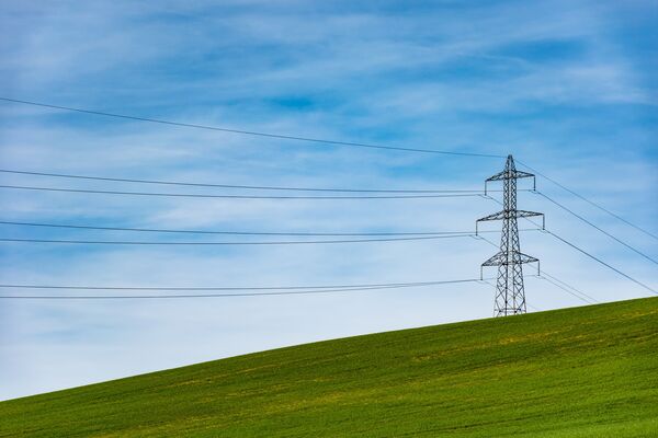Ein Strommast steht auf einer grünen Wiese vor blauem Himmel.