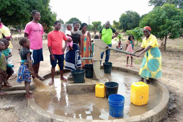 Menschen aus Mosambik stehen an einem neuen Brunnen und eine Frau pumpt Wasser.
