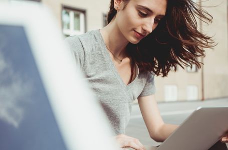 junge Frau mit Laptop auf dem Schoss tippt etwas auf der Tastatur