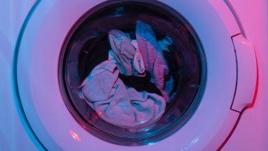 Eine Waschmaschine, die in neonfarbenen Licht angestrahlt wird. Man sieht Wäsche durch ein Fenster an der Tür der Waschmaschine.