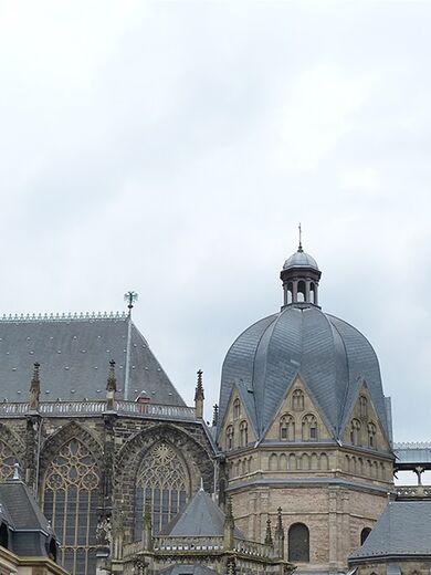 Der Aachener Dom mit seinem Turm vor einem Baum.