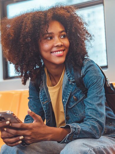 Eine junge, glückliche Frau die in einem leeren Zug sitzt und ein Smartphone in der Hand hält.