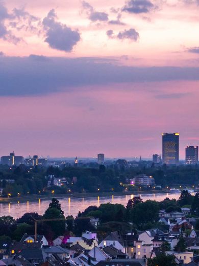 Die Skyline von Bonn mit dem Posttower und dem Rhein vor einem rötlichen Himmel