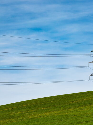 Ein Strommast steht auf einer grünen Wiese vor blauem Himmel.