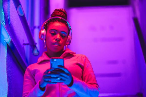 Frau steht im pinken Licht mit Kopfhörern auf und schaut auf ihr Handy