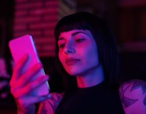 Frau mit schwarzen Haaren und Tattoos schaut auf ihr Handy