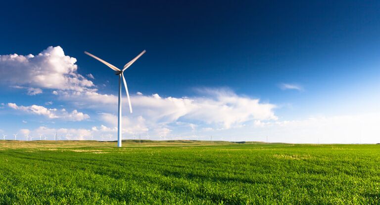 Windrad auf einer grünen Wiese vor blauem Himmel