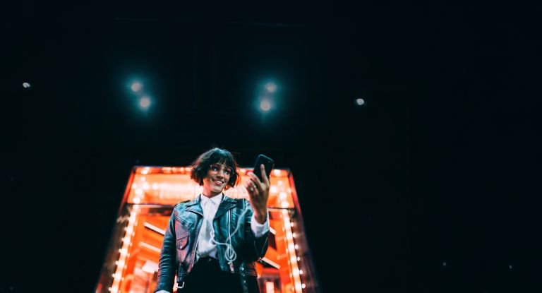 Eine Frau steht mit einem Handy in der Hand vor einem Neongebäude