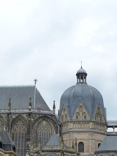 Der Aachener Dom mit seinem Turm vor einem Baum.