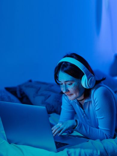 Eine Frau mit Kopfhörern liegt auf einem Bett mit einem Laptop.