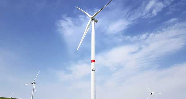 Drei Windräder auf einer grünen Wiese bei blauem Himmel.