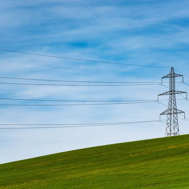 Ein Strommast steht auf einer grünen Wiese vor blauem Himmel.