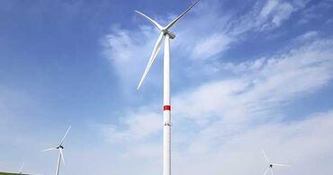 Drei Windräder auf einer grünen Wiese bei blauem Himmel.