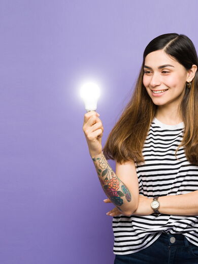 Eine lächelnde Frau hält eine leuchtende Glühbirne in der Hand