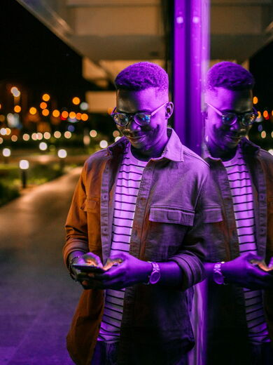 Mann mit Brille lehnt gegen Wand und schaut auf sein Handy