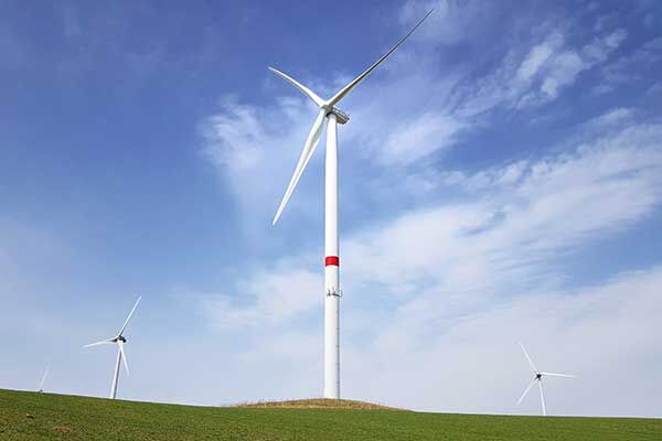 Drei Windräder auf einer grünen Wiese bei blauem Himmel.