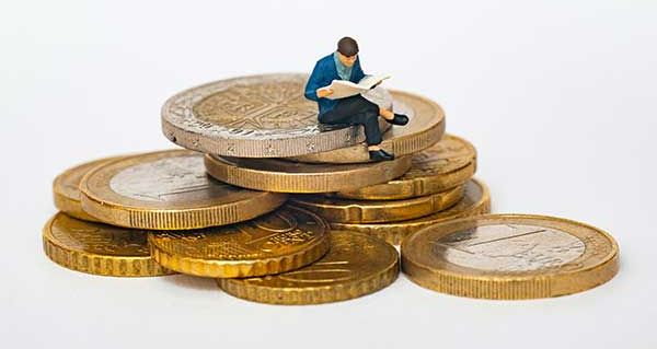 Figur auf Münzen Eine kleine Figur sitzt auf Geldmünzen und ließt eine Zeitung.