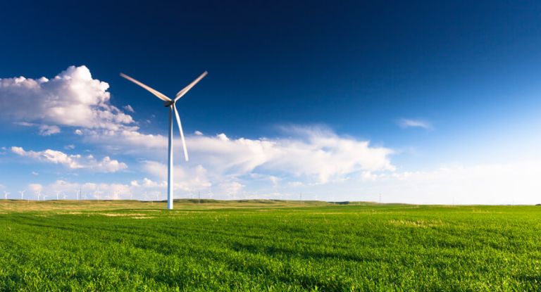 Windrad auf einer grünen Wiese vor blauem Himmel