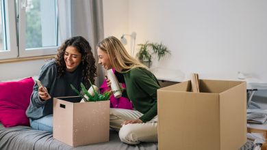 Zwei Frauen sitzen lächelnd auf einem Bett mit Umzugskartons