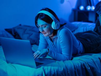 Frau auf dem Bett mit Laptop Eine Frau mit Kopfhörern liegt auf einem Bett mit einem Laptop.