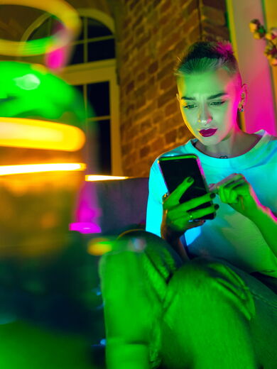 Eine grün angeleuchtete Frau sitzt mit ihrem Smartphone in der Hand auf einem Sofa