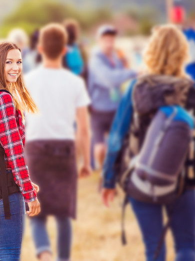 Mehrere Personen gehen über ein Feld zu einem Festival und eine Frau dreht sich lächelnd zur Kamera