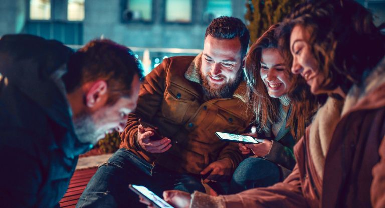 Vier lächelnde Freundinnen und Freunde mit Smartphones in der Hand