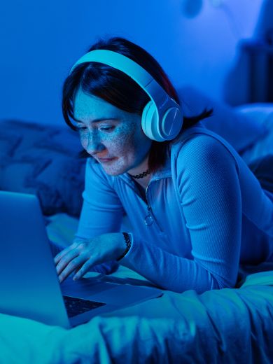 Eine Frau mit Kopfhörern liegt auf einem Bett mit einem Laptop.