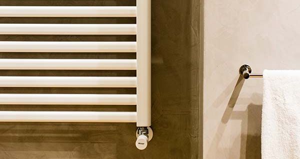 Ein weißer Handtuchheizkörper hängt vor einer braunen Wand und rechts davon ein Handtuchhalter mit einem weißen Handtuch.