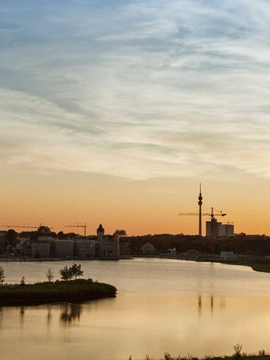 Die Stadt Dortmund bei Dämmerung hinter einem See.