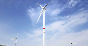 Drei Windräder auf einer grünen Wiese bei blauem Himmel.