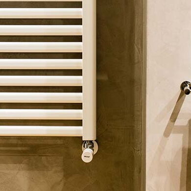 Ein weißer Handtuchheizkörper hängt vor einer braunen Wand und rechts davon ein Handtuchhalter mit einem weißen Handtuch.