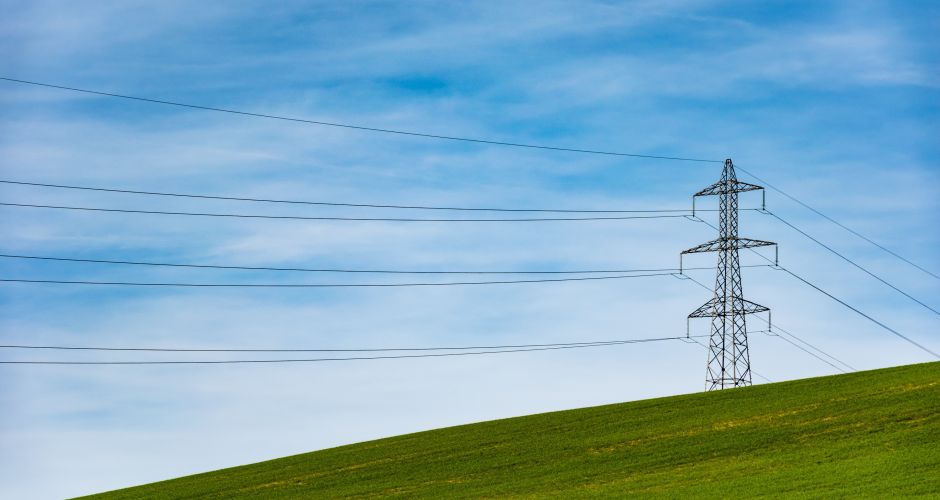 Ein Strommast steht auf einer grünen Wiese vor blauem Himmel.