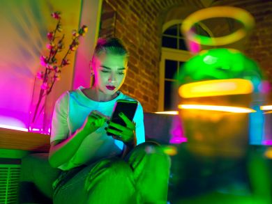 Eine Frau sitzt mit einem Handy auf der Couch und ist umgeben von Neonlichtern