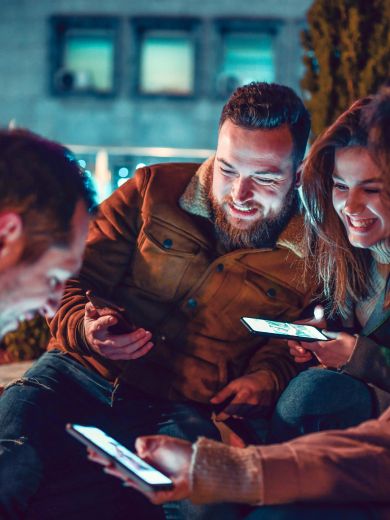 Vier lächelnde Freundinnen und Freunde mit Smartphones in der Hand