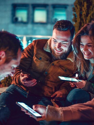 Vier lächelnde Freundinnen und Freunde mit Smartphones in der Hand