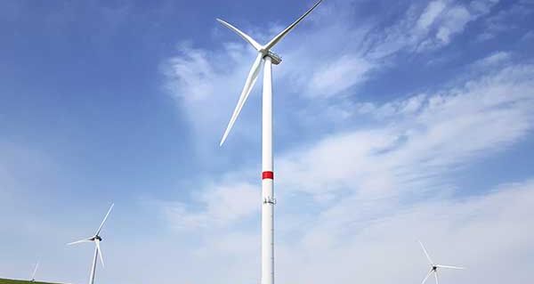 Drei Windräder auf einer grünen Wiese bei blauem Himmel.