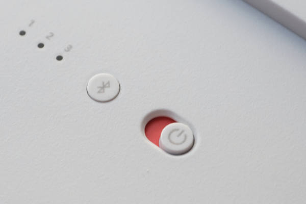 auf einem weißen Gerät befindet sich ein An- und Ausschlater, welcher auf rot geschaltet ist und ein Bluetooth Schalter. Links davon befindet sich eine Nummerierung von 1-3 mit jeweils einem schwarzen Kreisen darunter.